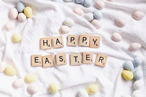 Barevná malovaná vajíčka ležící kolem nápisu na dřívkách Happy Easter.