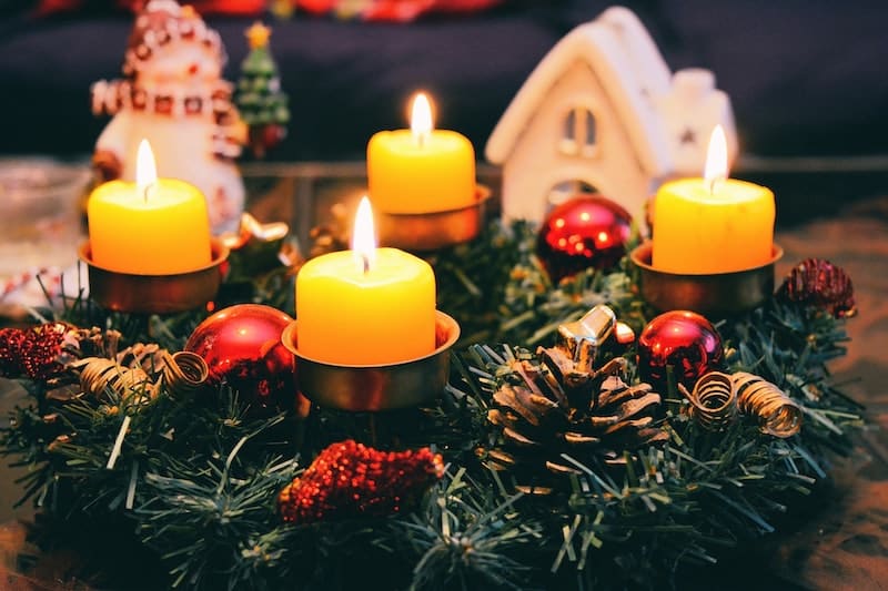 vánoční adventní věnec s čtyřmi hořícími svíčkami na svátečním stole, v pozadí jsou vánoční dekorace
