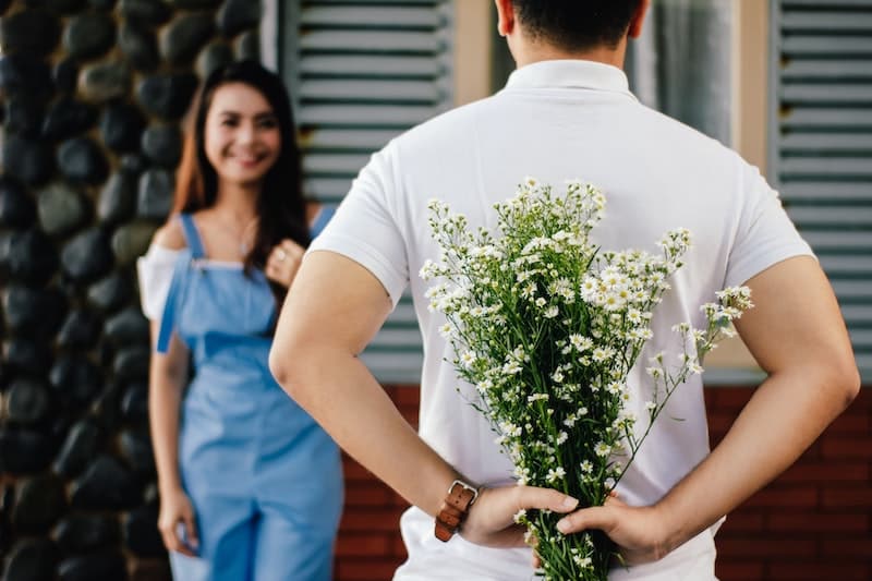 muž drží květinu za zády, žena se na něj směje