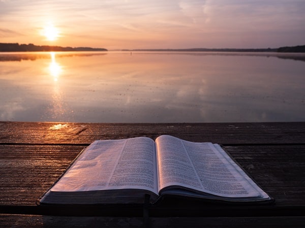 Bible ležící na molu u jezera při západu slunce