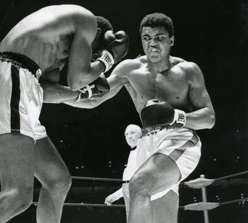Černobílá fotografie mladého boxujícího Muhammeda Aliho v ringu.