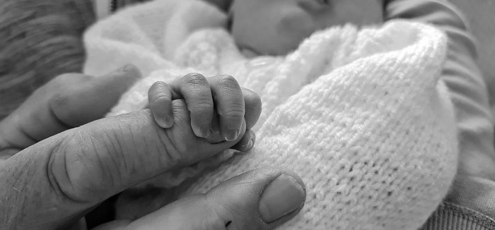 Černobílá fotografie ručky malého miminka, držící prst dospělé starší osoby.