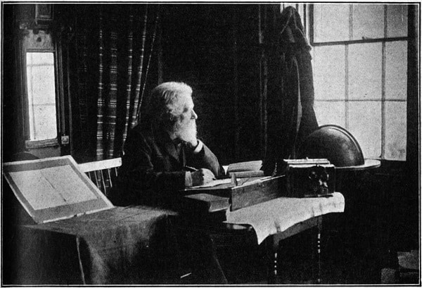 Černobílá fotografie Philipa Jamese Baileyho sedícího za stolem.