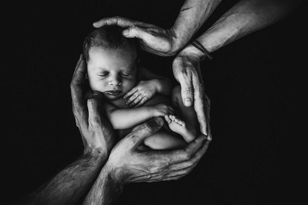 Černobílé přání k narození dcery s detailem na spící miminko obklopené mužskými a ženskými dlaněmi.