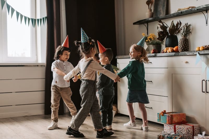 Čtyři děti - dva chlapci a dvě díky, slaví v pokoji narozeniny a mají veselé čepice.