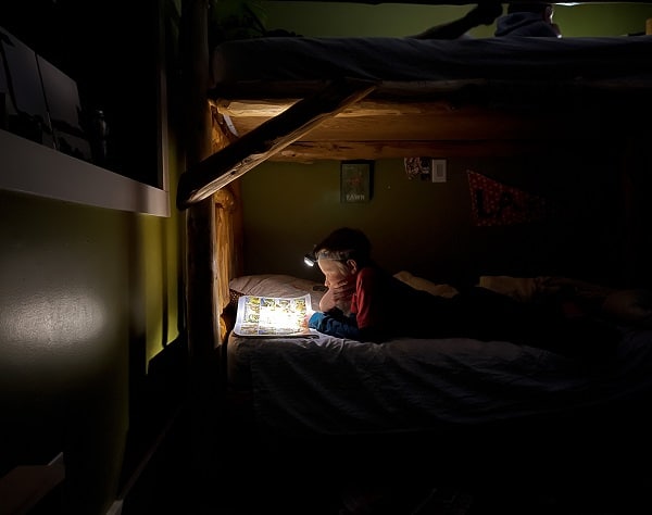 Chlapec čtoucí si knihu s baterkou na čele v posteli