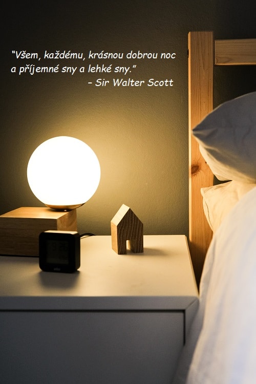Citát na dobrou noc od Sira Waltera Scotta na pozadí fotografie nočního stolku s lampičkou u postele.