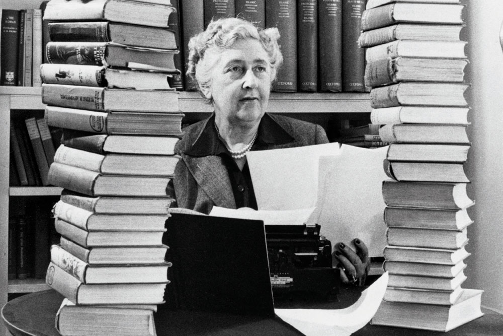 Agatha Christie sedí mezi stohy svých knih.