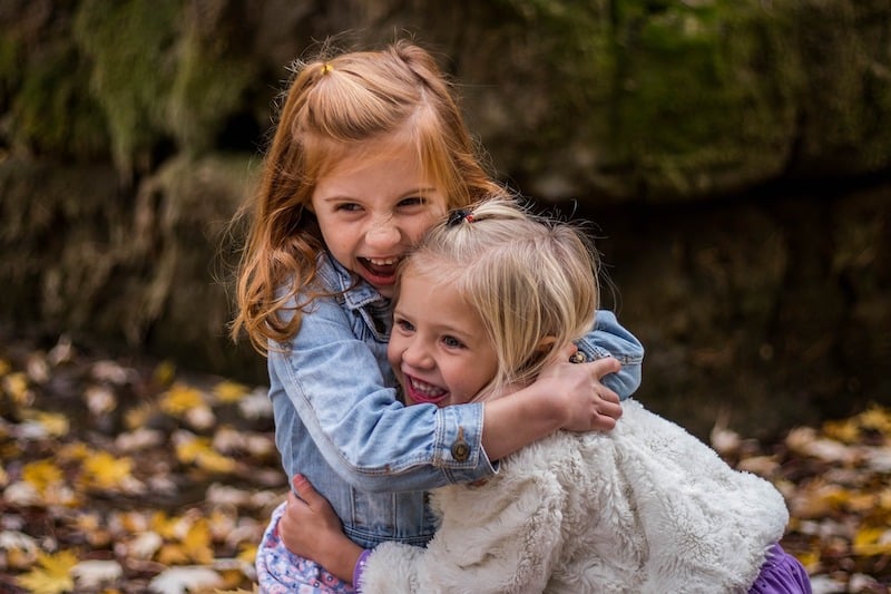 Dvě malé holky se vesele smějí a objímají v detailu.