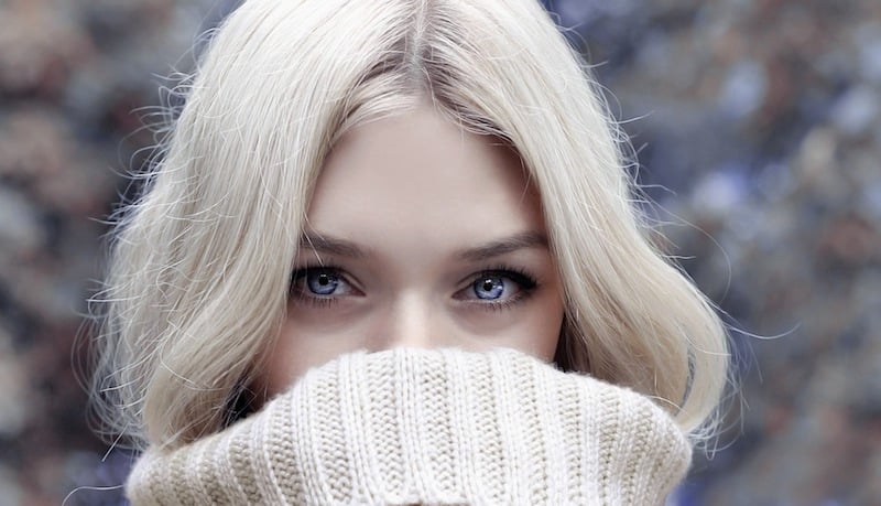 Mladá žena ve vlněném světlém svetru, koukají jen modré oči.