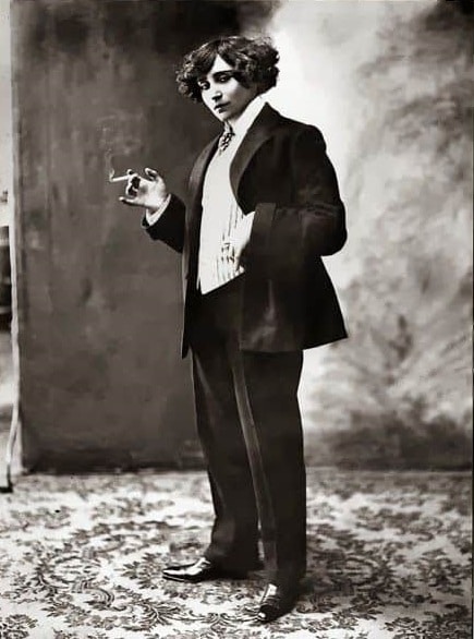 Stojící Colette v pánském obleku s cigaretou v ruce