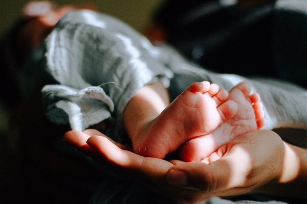 Fotografie dospělé dlaně držící malé nožky miminka. 
