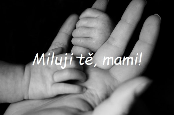 Černobílá fotografie dámské dlaně, kterou drží za prst dvě ruce miminka s nápisem "Miluji tě, mami!".