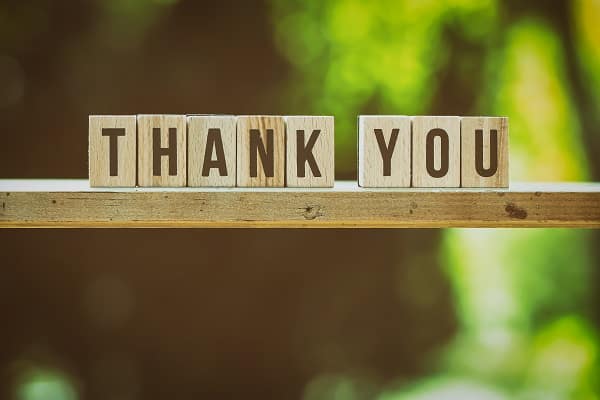 Dřevěné kostky s nápisem "thank you" na rozmazaném pozadí lesa.