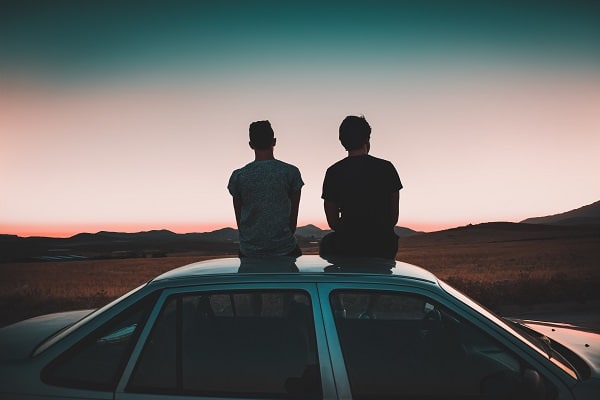 Dva muži sedící na střeše auta s výhledem na obzor při západu slunce.