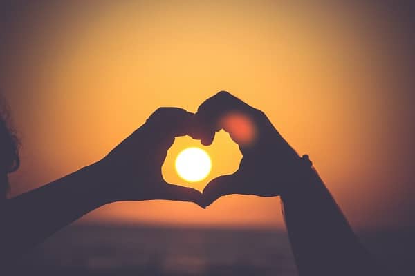Dvě spojující se dlaně do tvaru srdce, v jejichž středu je zapadající slunce.