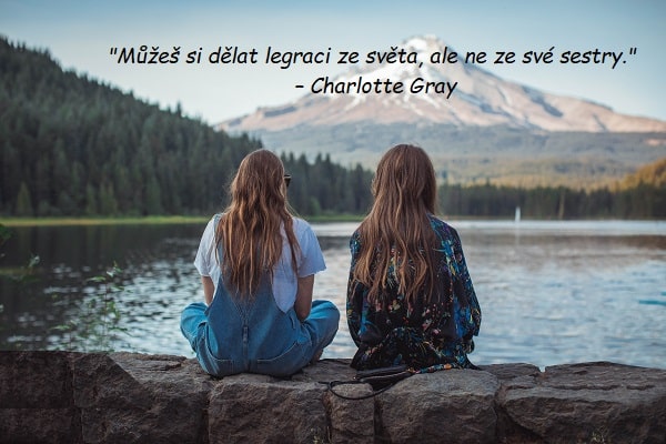 Citát o sestře od Charlotte Gray na pozadí zády sedících dívek na břehu jezera s výhledem na les pod horou.