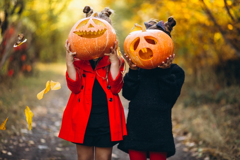 Dvě holky jsou převlečené v halloweenském kostýmů a drží si dýně před obličejem,