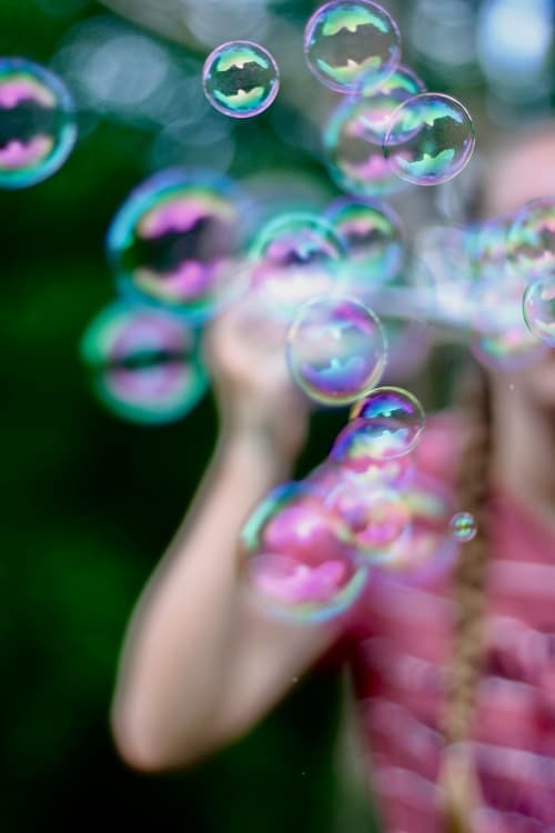 Dívka v růžovém tričku foukající bubliny z bublifuku.