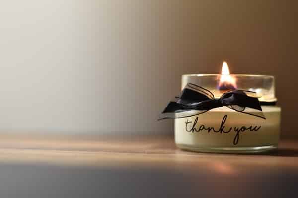 Poděkování za přání na sklenici s hořící svíčkou s nápisem "thank you" a s černou mašlí.