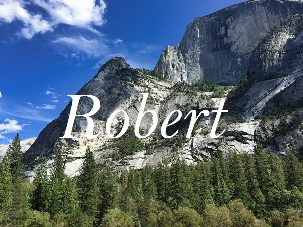 Jméno "Robert" na pozadí fotografie skály obklopené lesy pod modrou oblohou.