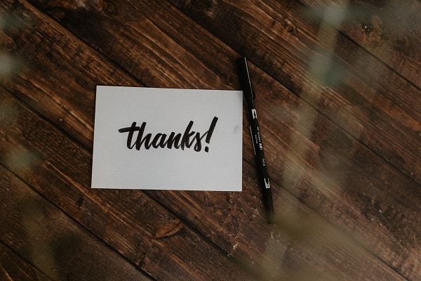 Bílá kartička s nápisem "Thanks!" a perem na dřevěném pozadí.