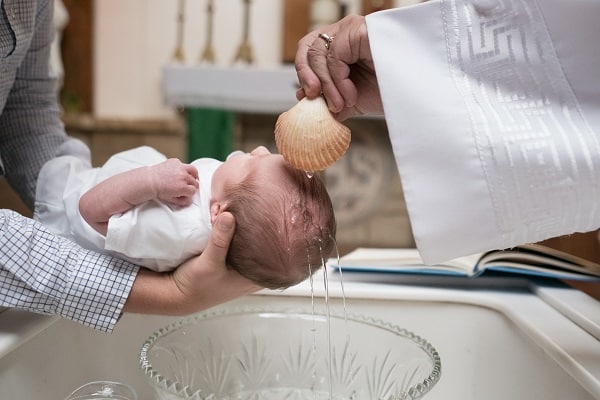 Ruka kněze polévající vodou miminko při křtu