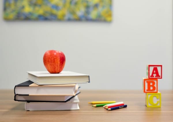 Knihy, kostky s písmeny a pastelky s jablkem na školní lavici.