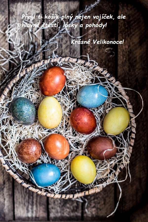 Barevná malovaná velikonoční vajíčka v košíku vystlaném slámou a s blahopřáním k velikonočním svátkům.