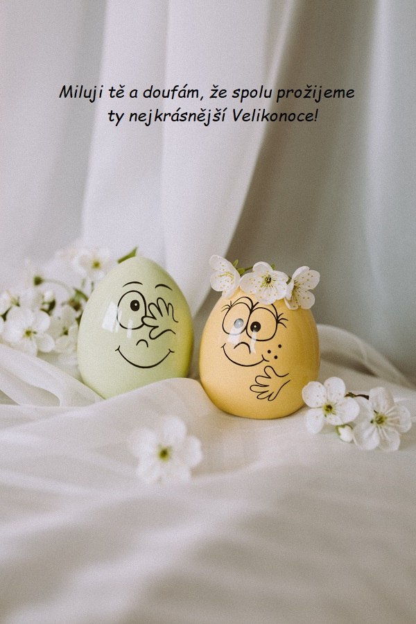 Zelené a žluté vajíčko s nakreslenými usmívajícími se obličeji, zdobená bílými květy. 