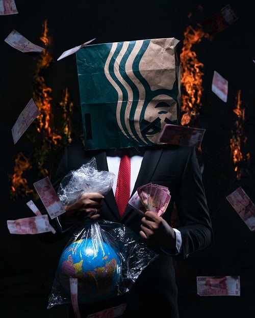 Muž v obleku s papírovou taškou na hlavě a s penězi v ruce, na pozadí hořících plamenů