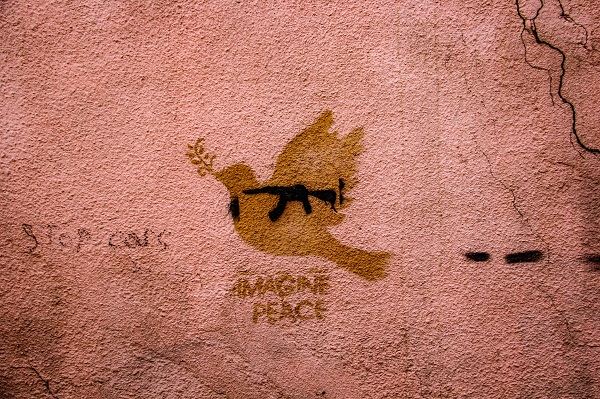 Holubice se samopalem namalovaná na zdi s nápisem "Imagine peace"