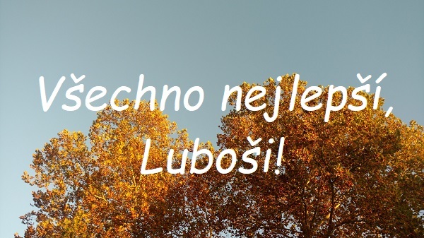 Nápis "Všechno nejlepší, Luboši!" na pozadí listnatých stromů se žlutými listy pod modrou oblohou.