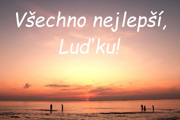 Nápis "Všechno nejlepší, Luďku!" na pozadí pláže s lidmi u moře při západu slunce.