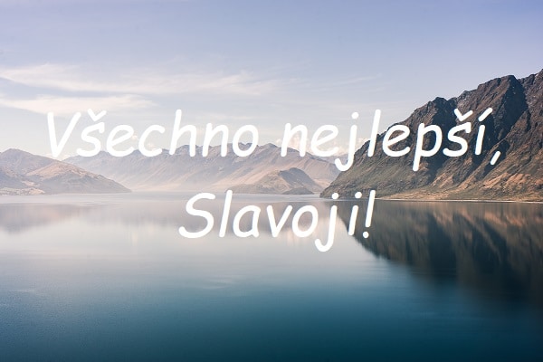 Nápis "Všechno nejlepší, Slavoji!" na pozadí jezera obklopeného horami.