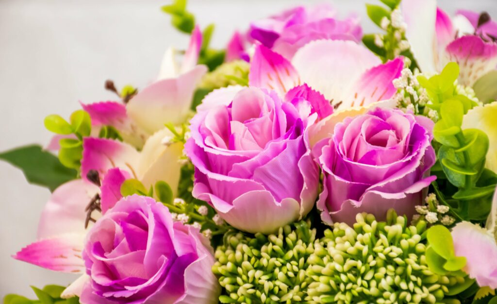 Kytice s růžovými růžemi a zelenými květinami.