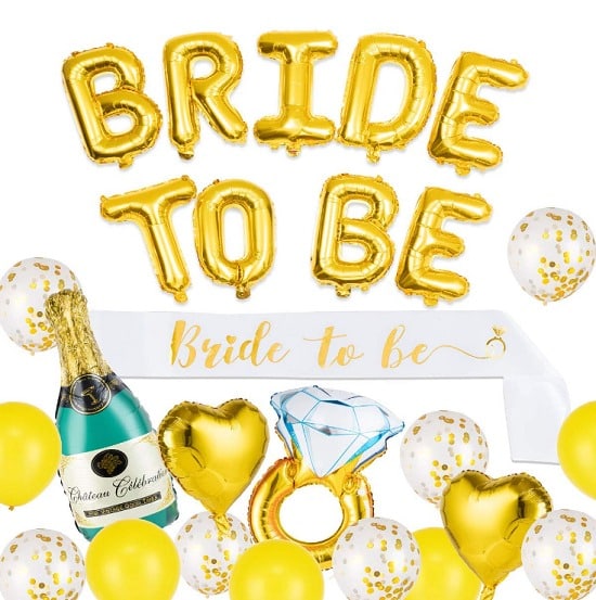 Pozvánka na rozlučkovou party se svobodou s nápisem "Bride to be" ze zlatých nafukovacích balónků, šampaňským a prstenem. 