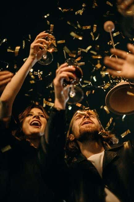 Oslavující skupina lidí s konfetami a se skleničkou v ruce. 