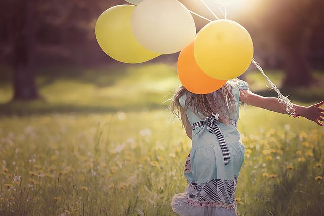 Přání k svátku s dívkou běžící po louce s balony.
