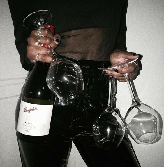 Holka drží v ruce víno a tři skleničky. 