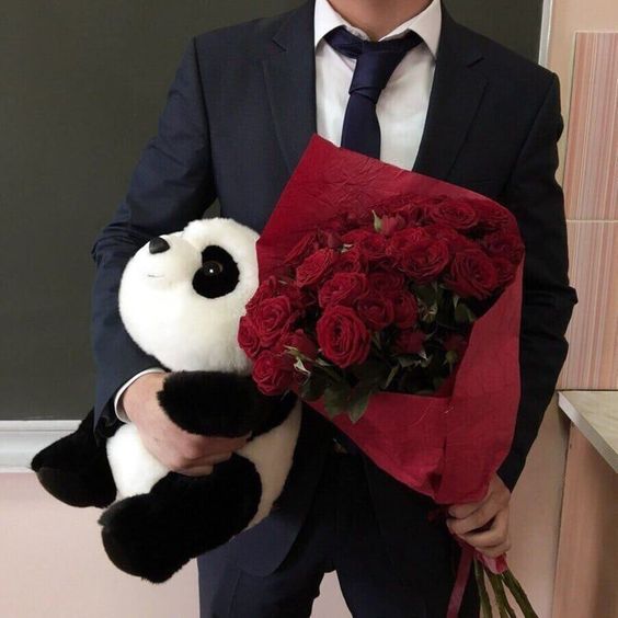 Muž v obleku s kyticí rudých růží a plyšovou pandou. 