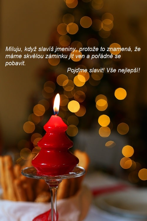 Hořící svíčka ve tvaru stromečku na pozadí vánočního stromu s přáním k svátku pro Ambrože.
