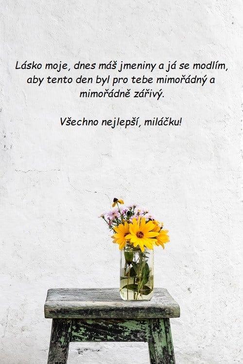 Váza s lučními květinami na dřevěném stolečku u bílé zdi se zamilovaným přáním ke jmeninám.