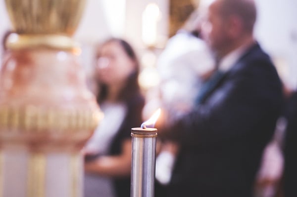 Rozmazaná fotografie rodičů s dítětem na křtinách v popředí se zaostřenou svíčkou