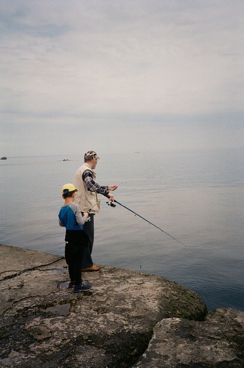 Rybařící starý muž s rybářským prutem a malým chlapcem na okraji moře.