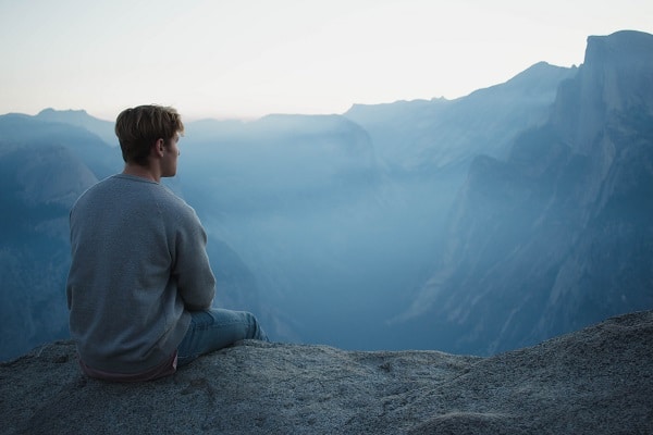 Sedící muž v přírodě, hledící na hory