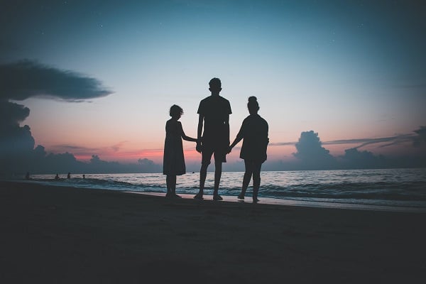 Silueta tří sourozenců na pláži při západu slunce.