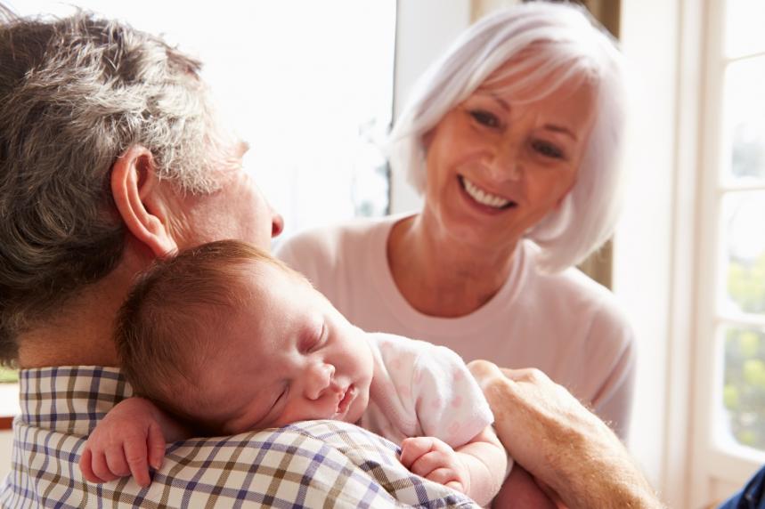 Smějící se prarodiče držící v náručí malé spící miminko.