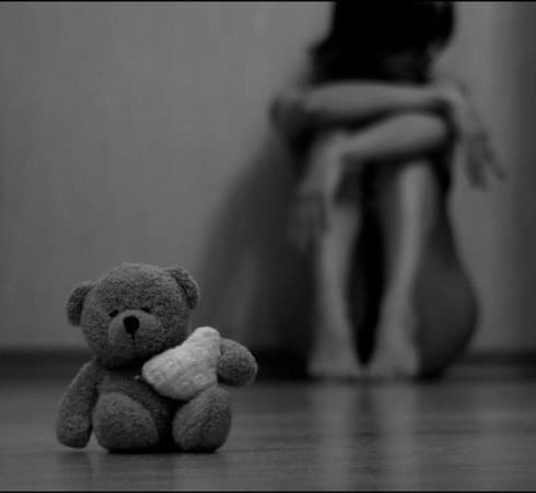 Černobílá fotografie smutné na zemi sedící ženy s plyšovým medvídkem