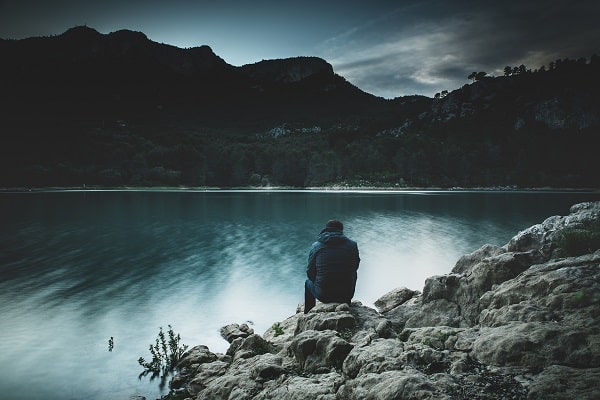 Smutně působící obrázek muže sedícího na okraji jezera